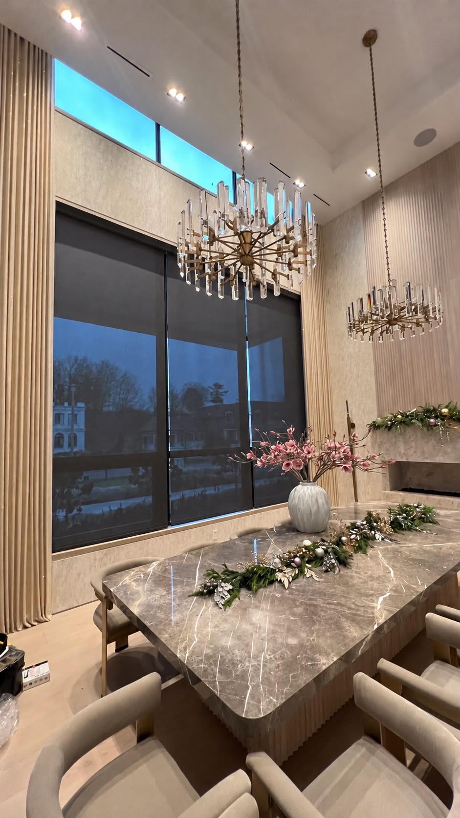 Dark roller shades layered with ivory drapery in a double-height dining room