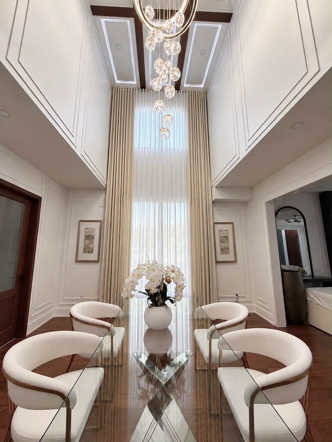 Floor-to-ceiling ivory drapery and sheer curtains in a double-height dining room